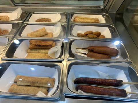 Snack case with corn dogs, egg rolls, and sausage on a stick